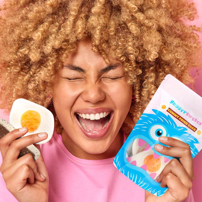 A joyful woman holding a Frosty Sweets Subscription Box 30 and a half-eaten gummy egg.